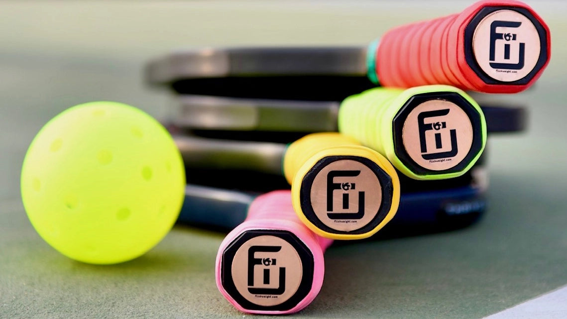 Flick Weight Banner Image - Flick Weights put on the bottom of Pickleball Paddles stacked up with PIckleball on a Court